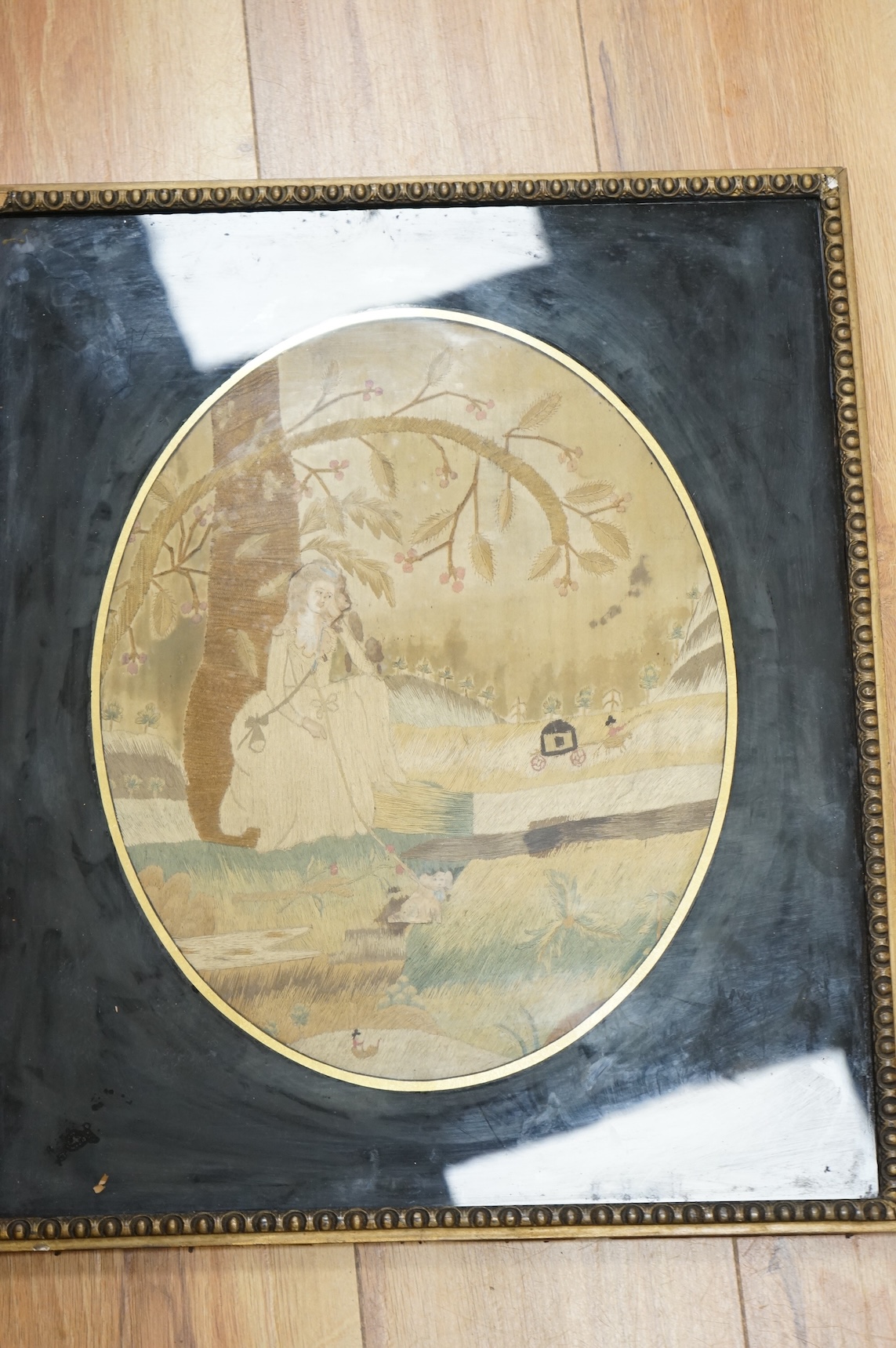 An early 19th century framed oval silk embroidery of a woman with a dog, overall 48cm high